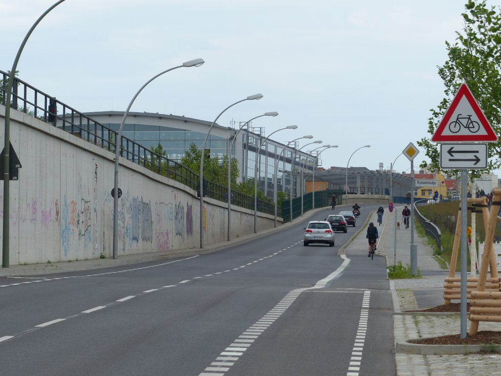 Kynaststra�e, Richtung Norden. Links im Bild die Ringbahnhalle des Bahnhofs Ostkreuz. Um Geld zu sparen, wurde die Br�cke �ber die Eisenbahn sehr eng gebaut. Und so gibt es nun einen nicht benutzungspflichtigen Radweg in Richtung Norden und keinen Radweg oder -streifen in Richtung S�den. Erst hinter der Br�cke, ganz links im Bild, beginnt ein Radstreifen. Nach wie vor gilt: In Engstellen, die besonderen Stress zwischen Auto- und Radfahrern herbeif�hren, werden keine Angebote f�r Radfahrer gemacht. Ist die Stra�e ausreichend breit, so dass es ohnehin keine nennenswerten Probleme gibt, wird ein Radstreifen aufgepinselt. 3.6.2013