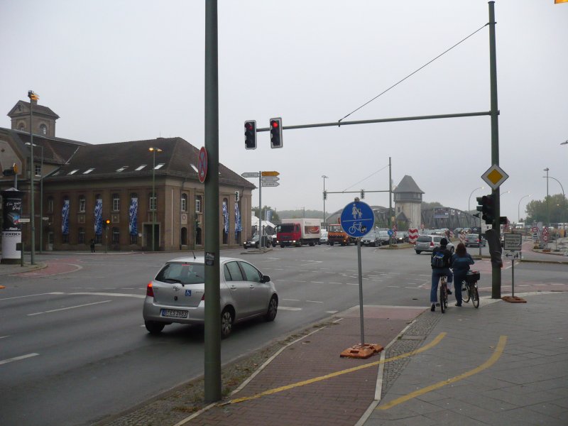 Damit Radfahrer nicht auf die Verkehrsinsel f�r linksabbiegende Radfahrer kommen, die ohne Ampel nur unter Gefahr nutzbar ist - hat man den Radweg gesperrt, und zwar mit einem Verkehrsschild: gemeinsamer Fu�- und Radweg! Ich musste etwas �berlegen, wie diese Speziall�sung gemeint ist und wie ich hier nach links abbiegen soll. Auf dem  gesperrten  Radweg soll man nicht weiterfahren, sondern die geradeausf�hrende Fu�g�ngerampel benutzen. Ich musste etwas nachdenken, bis ich darauf kam, die Radfahrer im Bild scheinen es auch nicht verstanden zu haben. Der Radweg schafft hier in Kombination mit der Baustelle eine Situation, die nur schwer zu �berblicken ist. Als Autofahrer merkt man davon nichts.