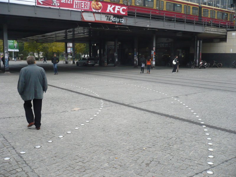 Designerradweg �ber den Alexanderplatz in Berlin. Nat�rlich funktioniert die gew�nsche Separierung zwischen Fu�g�ngern und Radfahrern hier �berhaupt nicht, da der angedeutete Weg entweder nicht wahrgenommen oder nicht als Radweg verstanden wird. Das h�tte man sich vorher denken k�nnen, sinnvoller w�re wohl eine Fu�g�ngerzone mit dem Zusatz  Radfahrer frei .